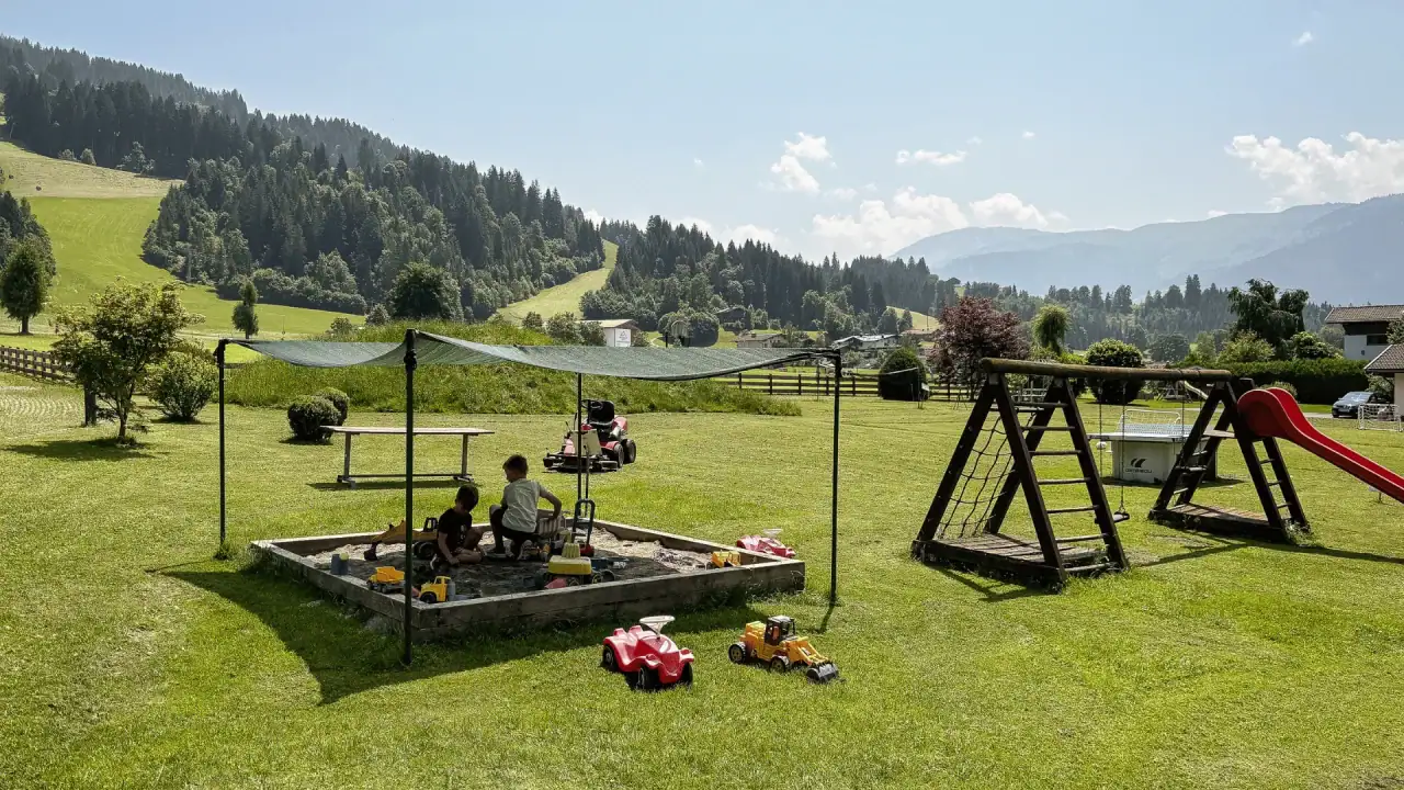 Kinder spielen im Sandkasten auf einer Wiese.