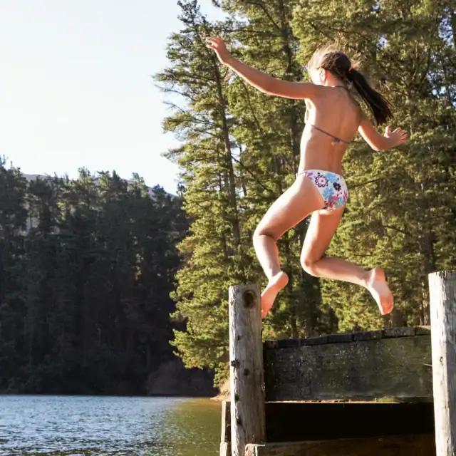 Mädchen springt vom Steg ins Wasser.