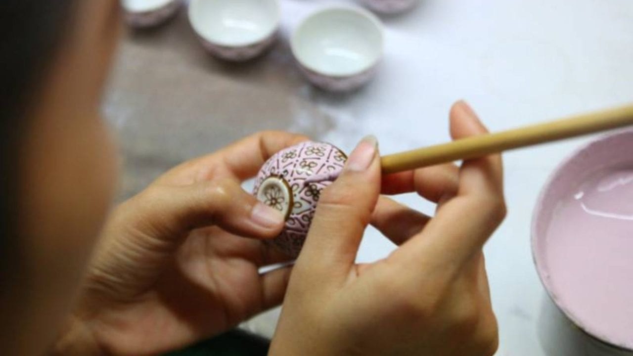 Hände bemalen eine kleine dekorative Schale.