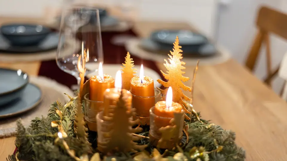 Adventskranz mit vier brennenden goldenen Kerzen auf festlichem Tisch