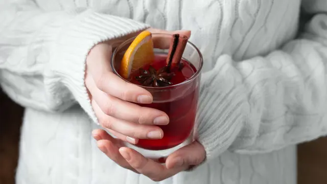 Hände im Strickpullover halten ein Glas Glühwein mit Gewürzen.