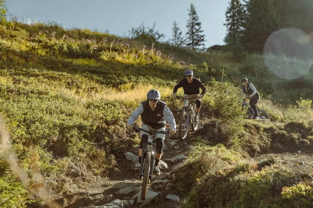 Drei Mountainbiker befahren einen steinigen Trail in den Bergen.